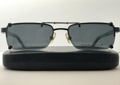 Spring bridge clip on sunglasses with gray lenses over Marchon M722, on top of a case
